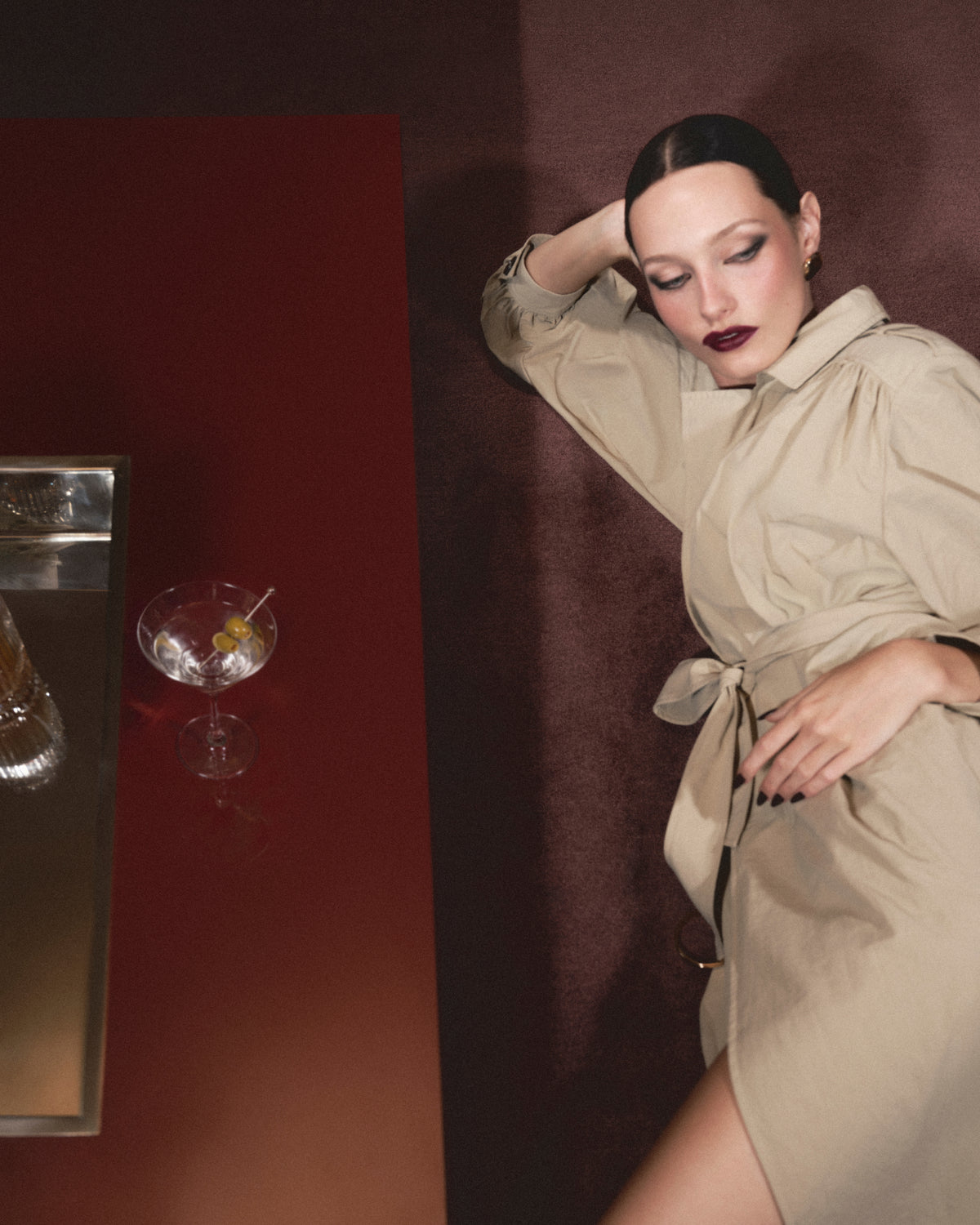 A woman wearing a deep red lipstick and blush lies on the floor next to a coffee table