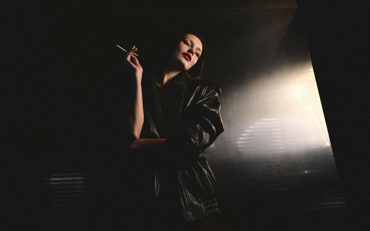 A woman wearing make-up, a bright red lipstick leans against a wall