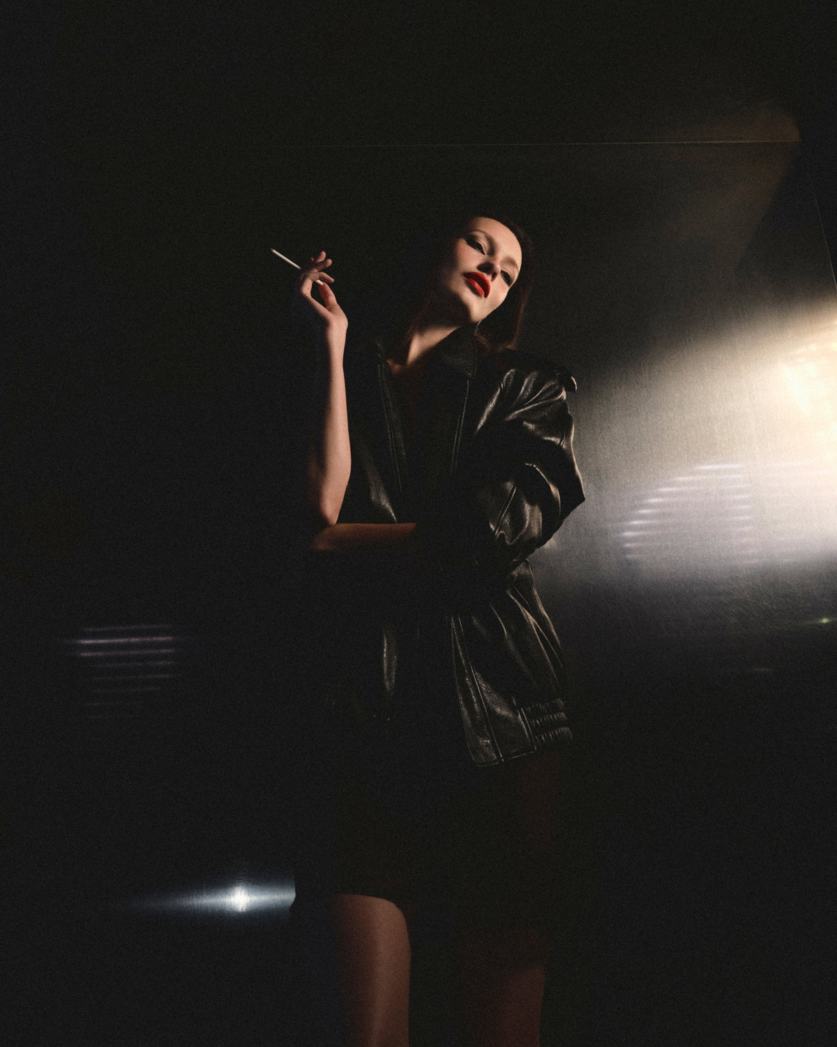 A woman wearing make-up, a bright red lipstick leans against a wall